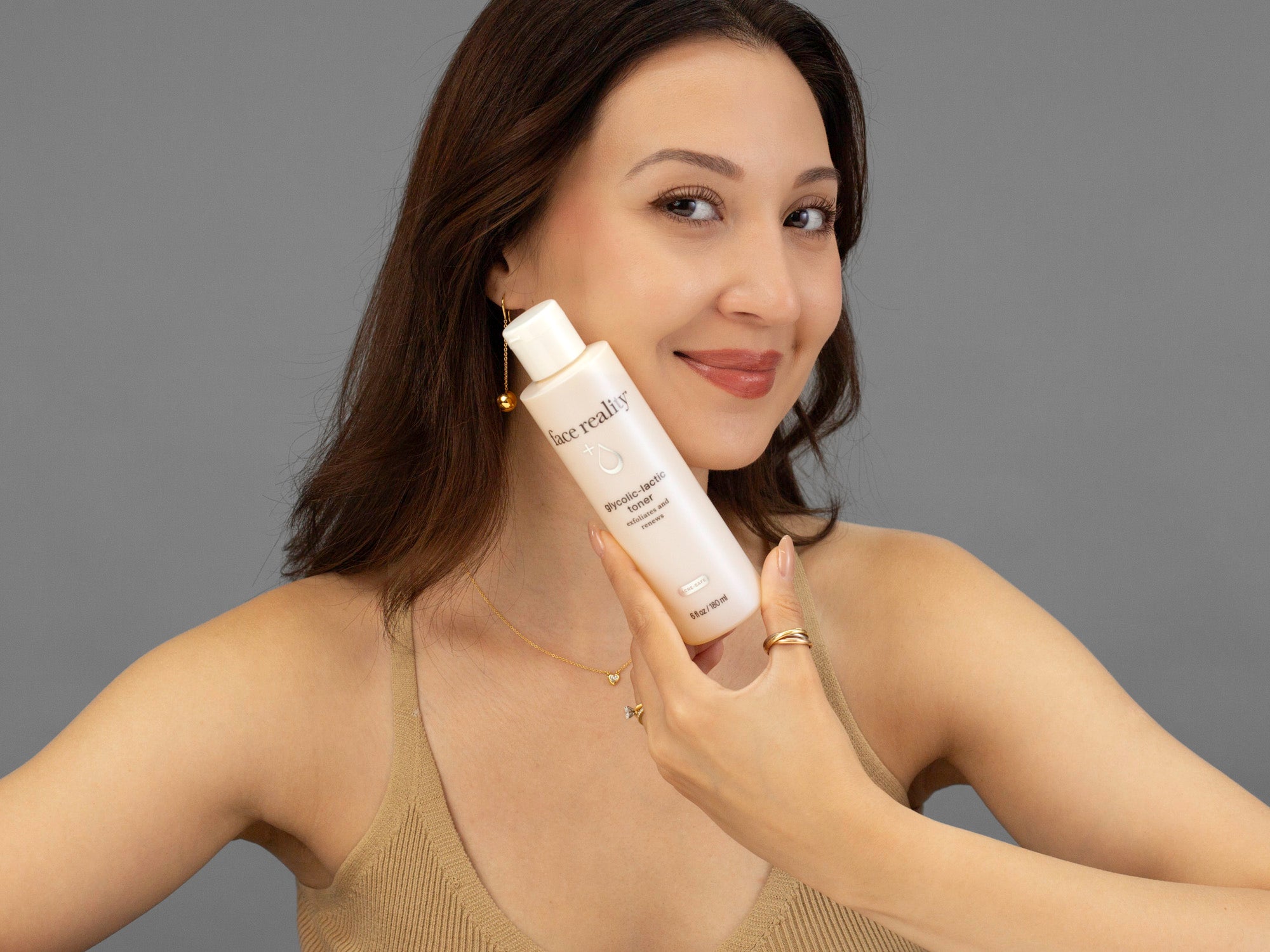 Laziza from LAZ Skincare holding a bottle of Face Reality Glycolic-Lactic Toner up to her face