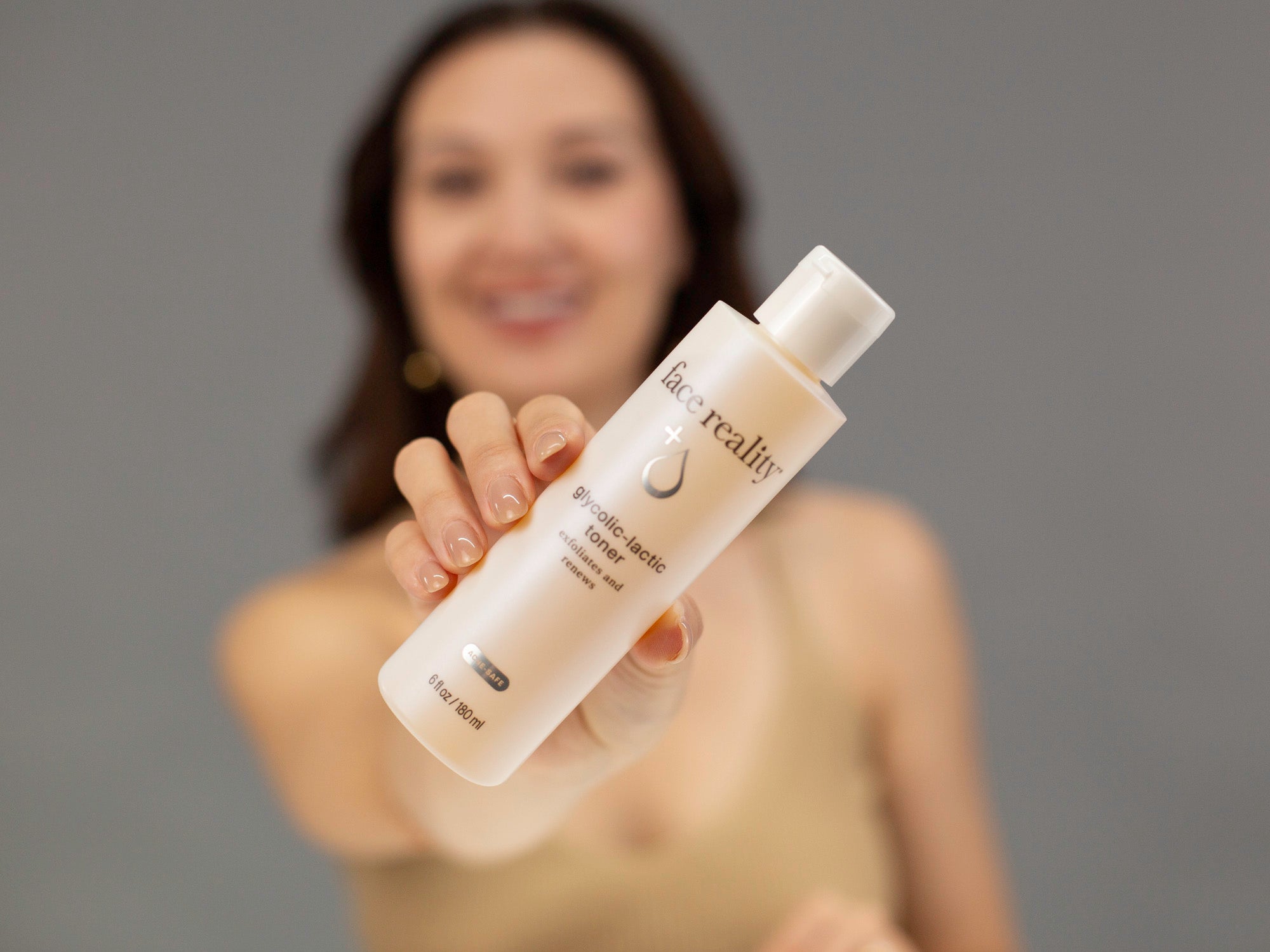 Laziza from LAZ Skincare holding up a bottle of Face Reality Glycolic-Lactic Toner with a blurred background