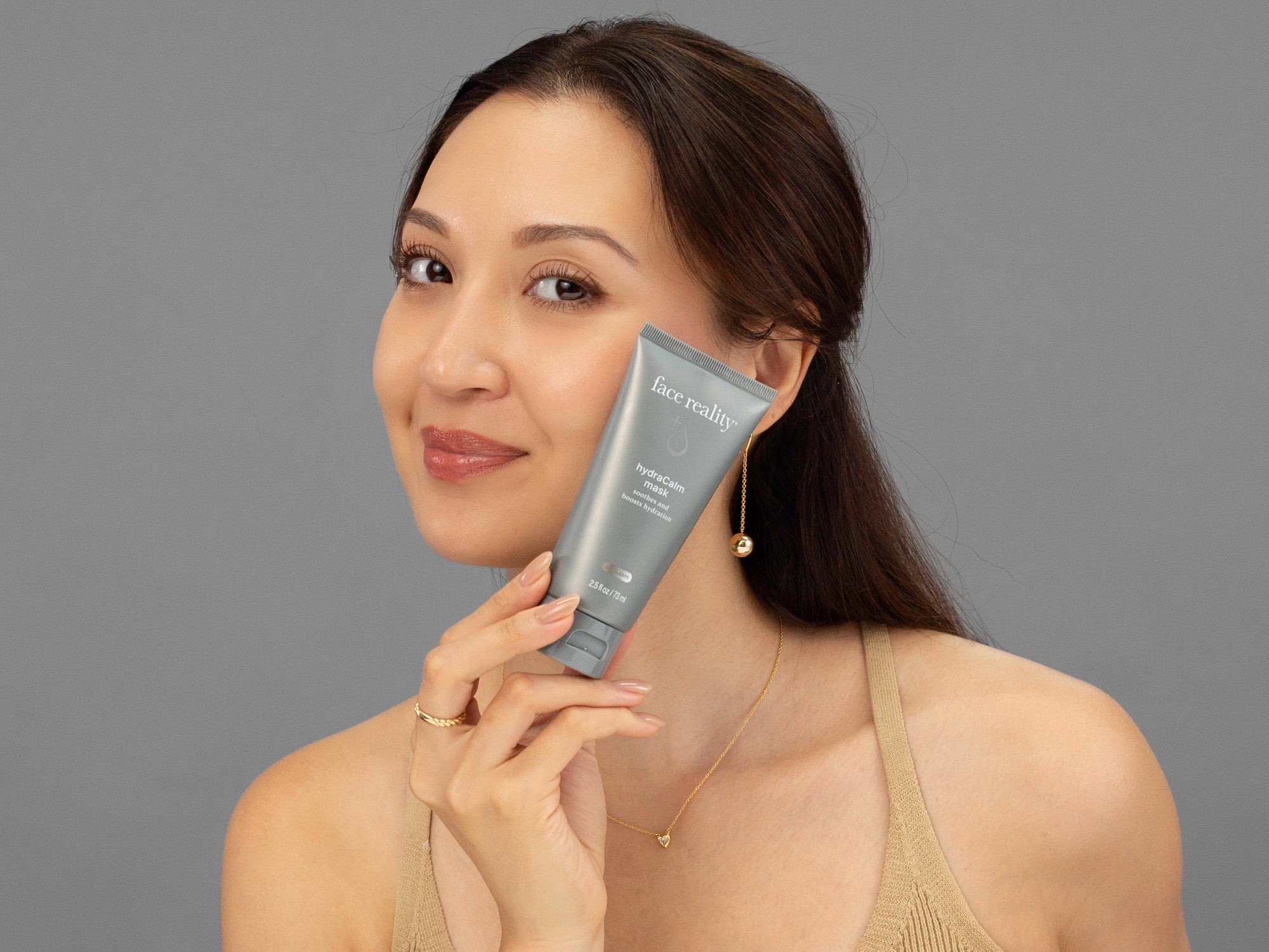 Laziza from LAZ Skincare holding a tube of Face Reality HydraCalm Mask up to her face