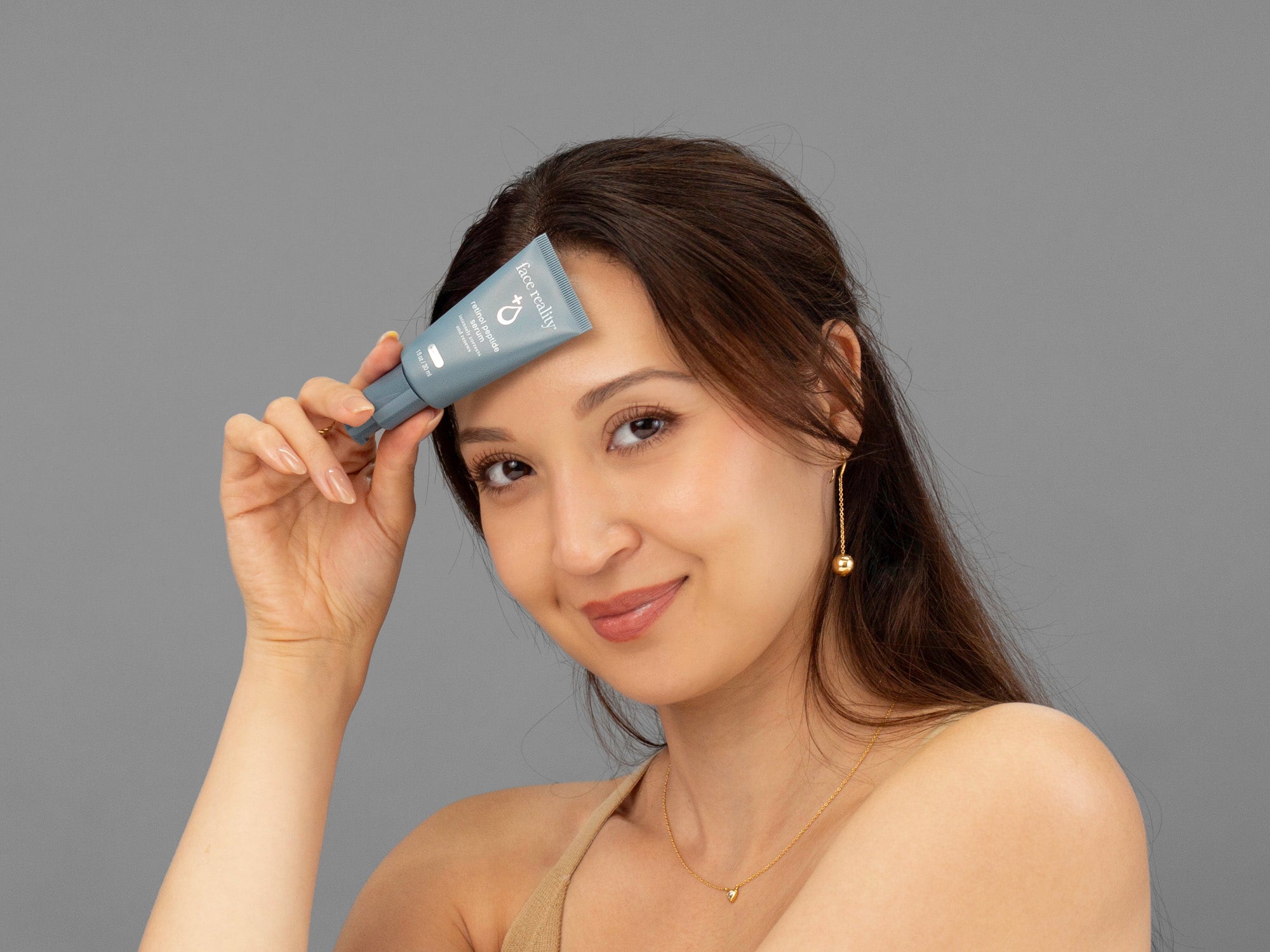 Laziza from LAZ Skincare holding a tube of Face Reality Retinol Peptide Serum up to her face