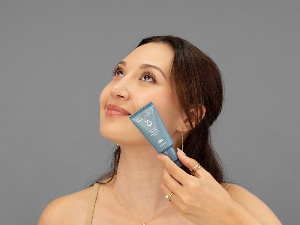 Laziza from LAZ Skincare holding a bottle of Face Reality Salicylic+ Serum up to her face