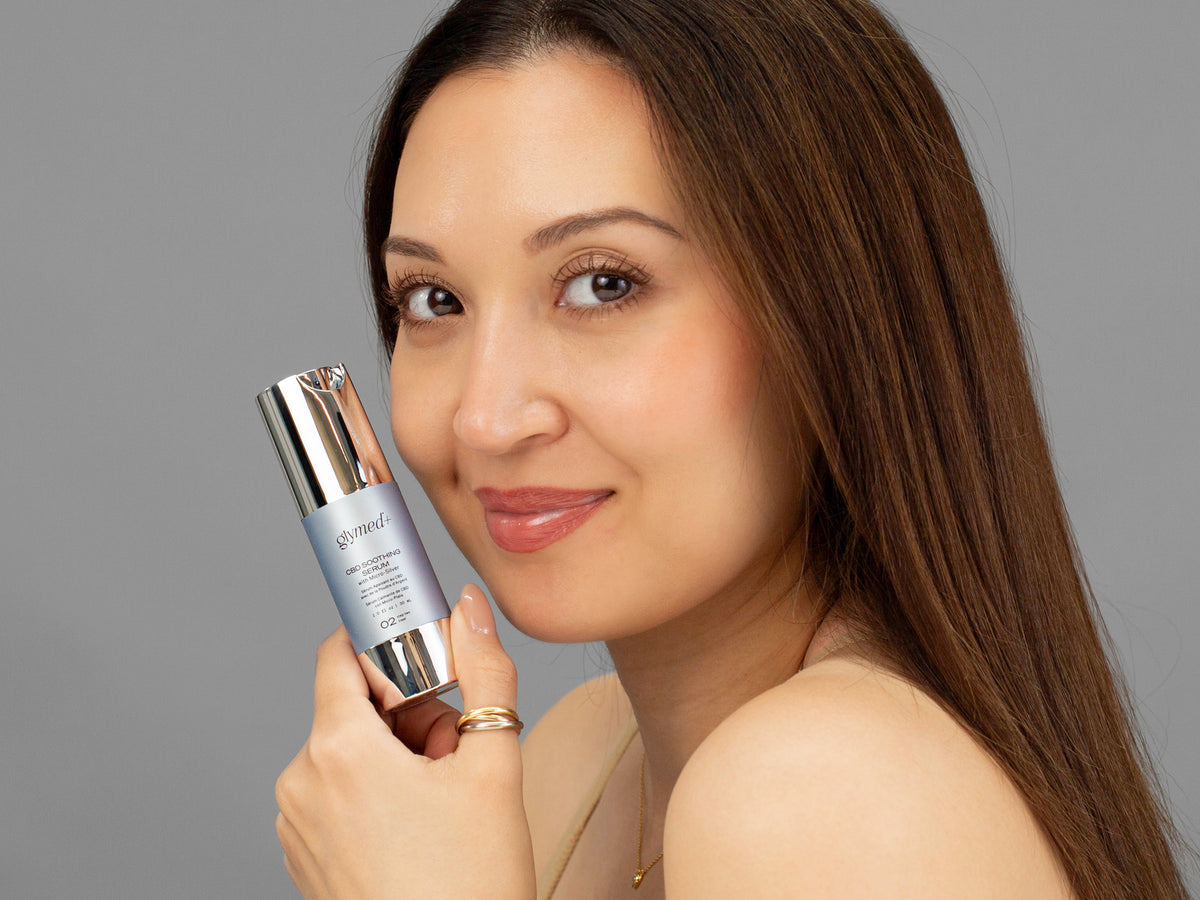 Laziza from LAZ Skincare holding a bottle of GlyMed Hemp Soothing Serum up to her face