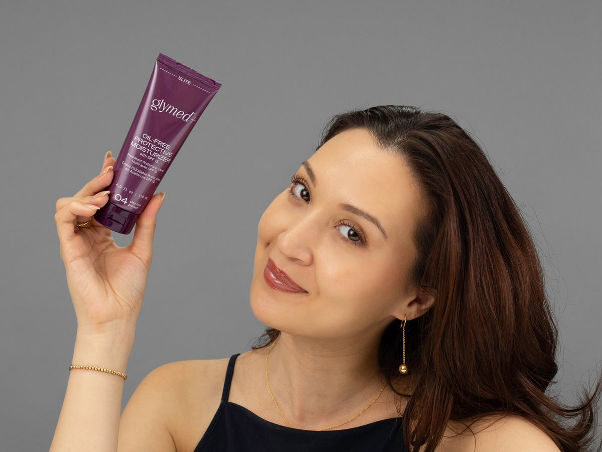 Laziza from LAZ Skincare holding a bottle of GlyMed Oil-Free Protective Moisturizer SPF 15 up to her face