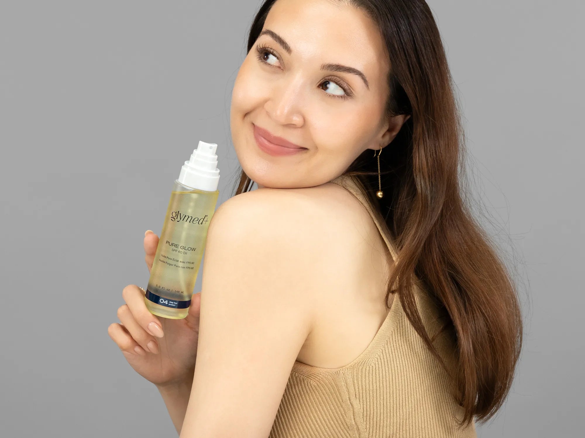 Laziza from LAZ Skincare holding a bottle of GlyMed Pure Glow SPF 60 Oil up to her face