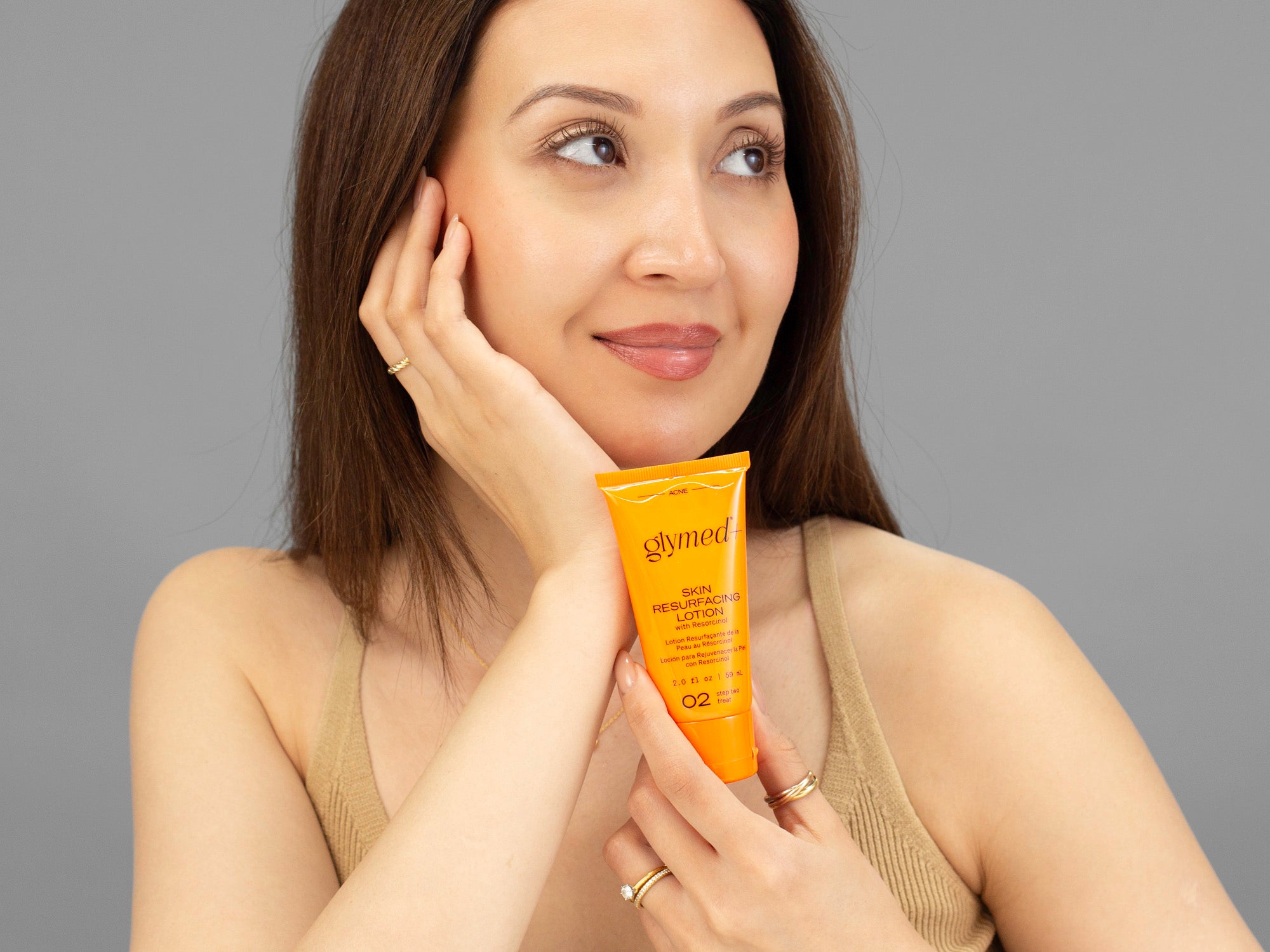 Laziza from LAZ Skincare holding a bottle of GlyMed Skin Resurfacing Lotion up to her face