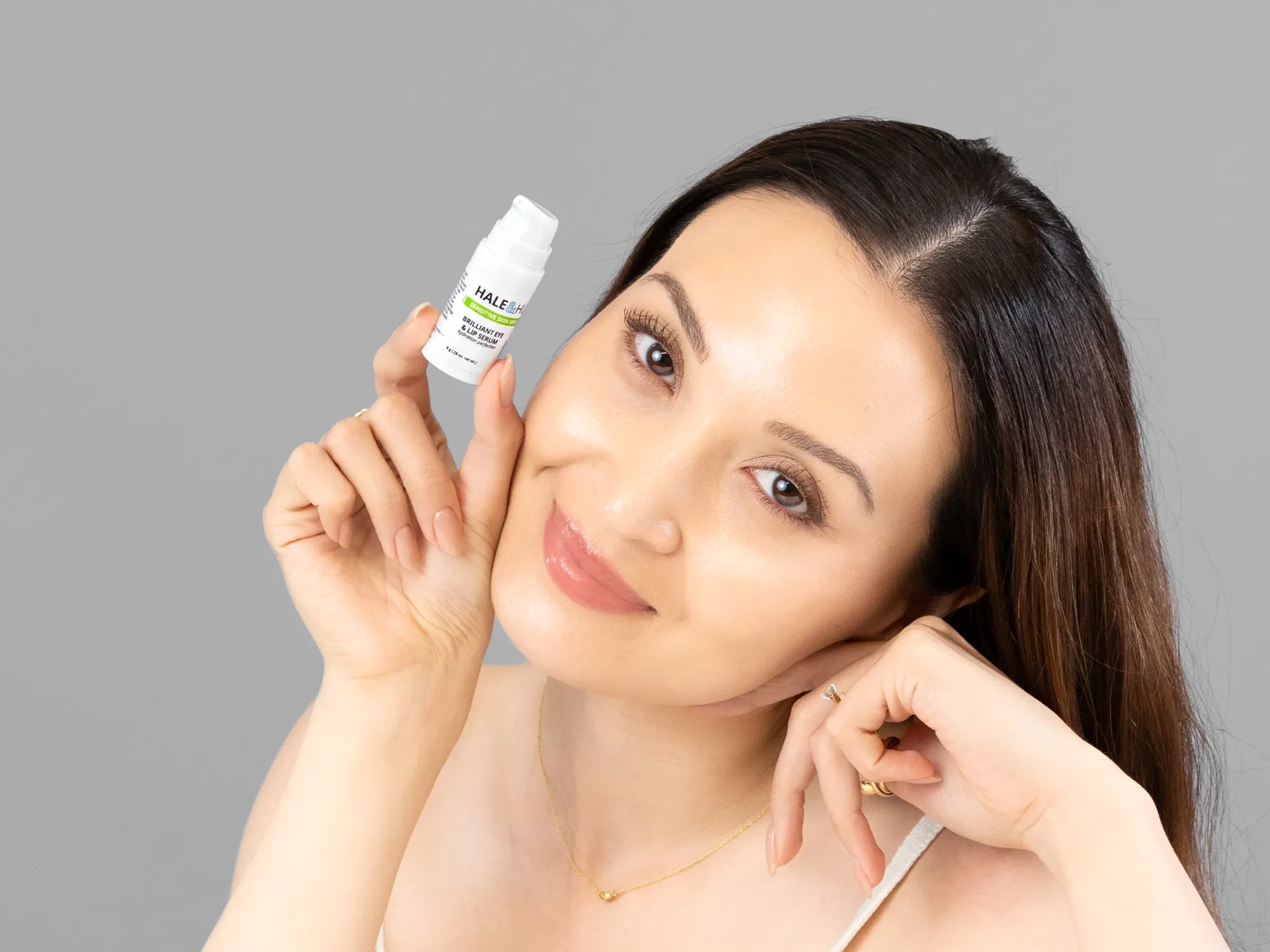 Laziza from LAZ Skincare holding a bottle of Hale & Hush Brilliant Eye & Lip Serum up to her face