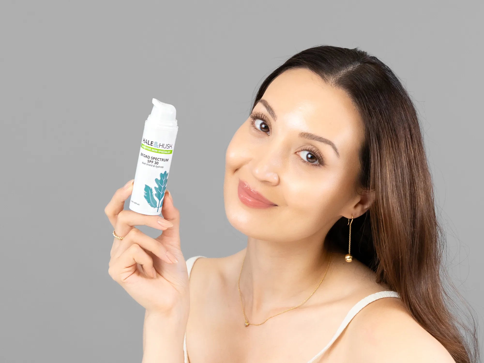 Laziza from LAZ Skincare holding a bottle of Hale & Hush Broad Spectrum Natural SPF30 up to her face