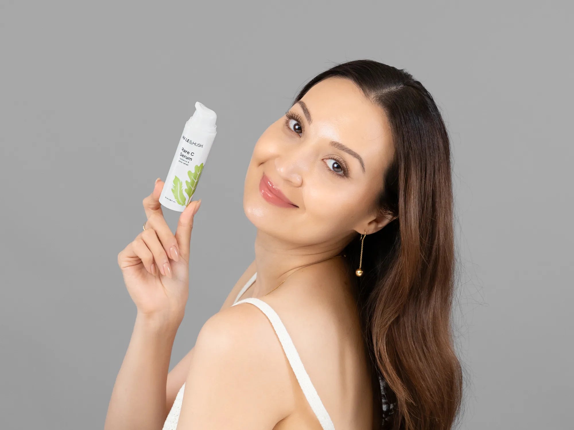 Laziza from LAZ Skincare holding a bottle of Hale & Hush Rare C Serum up to her face