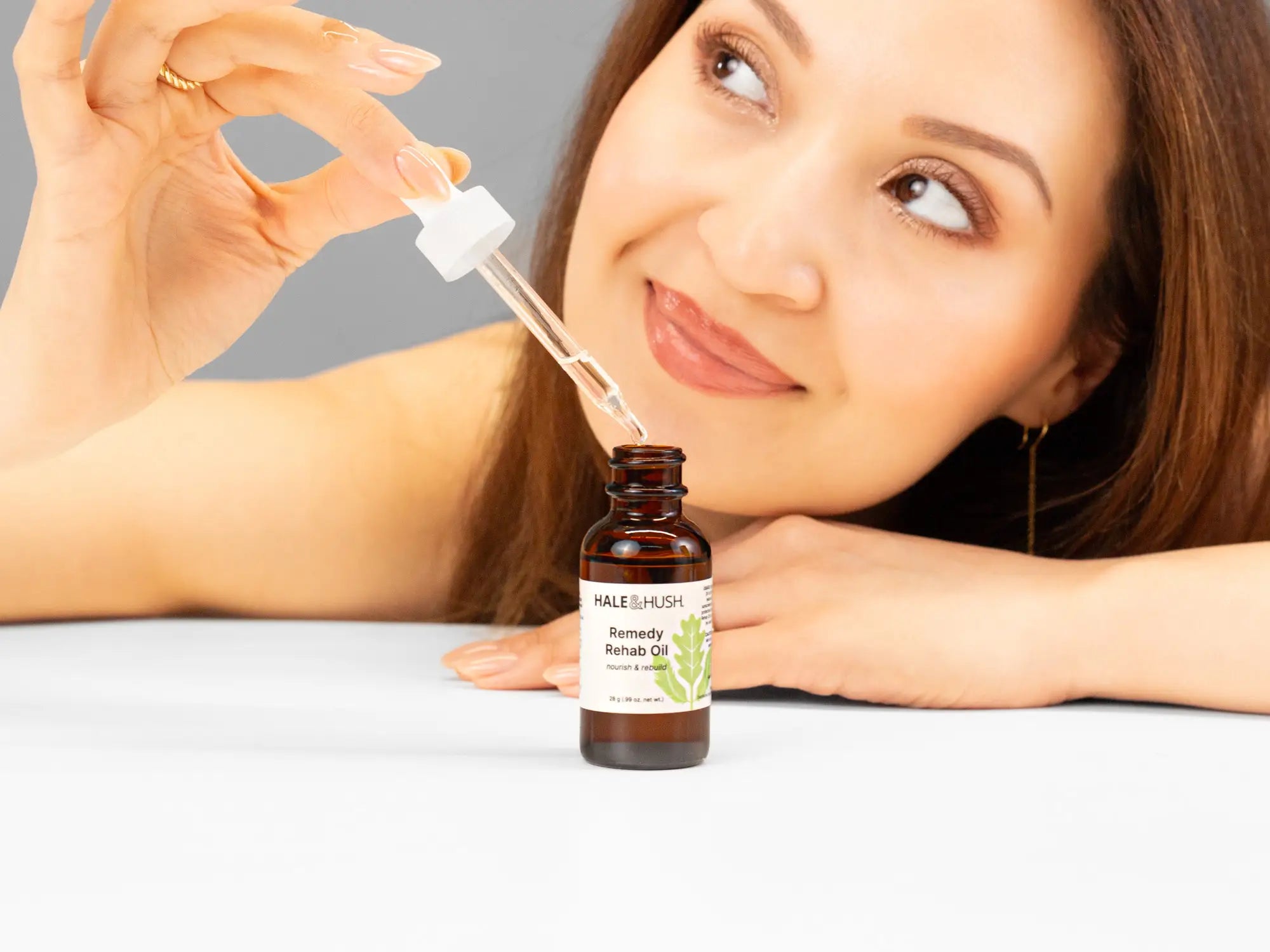 Laziza from LAZ Skincare holding a bottle of Hale & Hush Remedy Rehab Oil up to her face