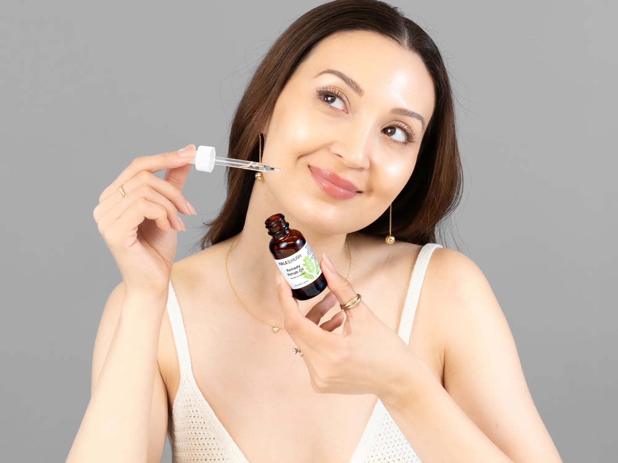 Laziza from LAZ Skincare holding a bottle of Hale & Hush Remedy Rehab Oil up to her face