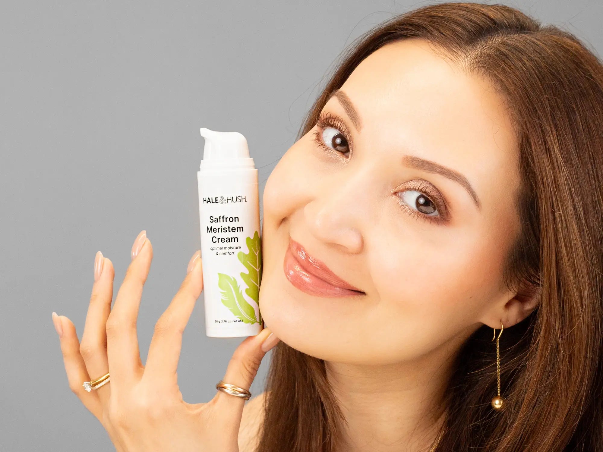 Laziza from LAZ Skincare holding a bottle of Hale & Hush Saffron Meristem Cream up to her face
