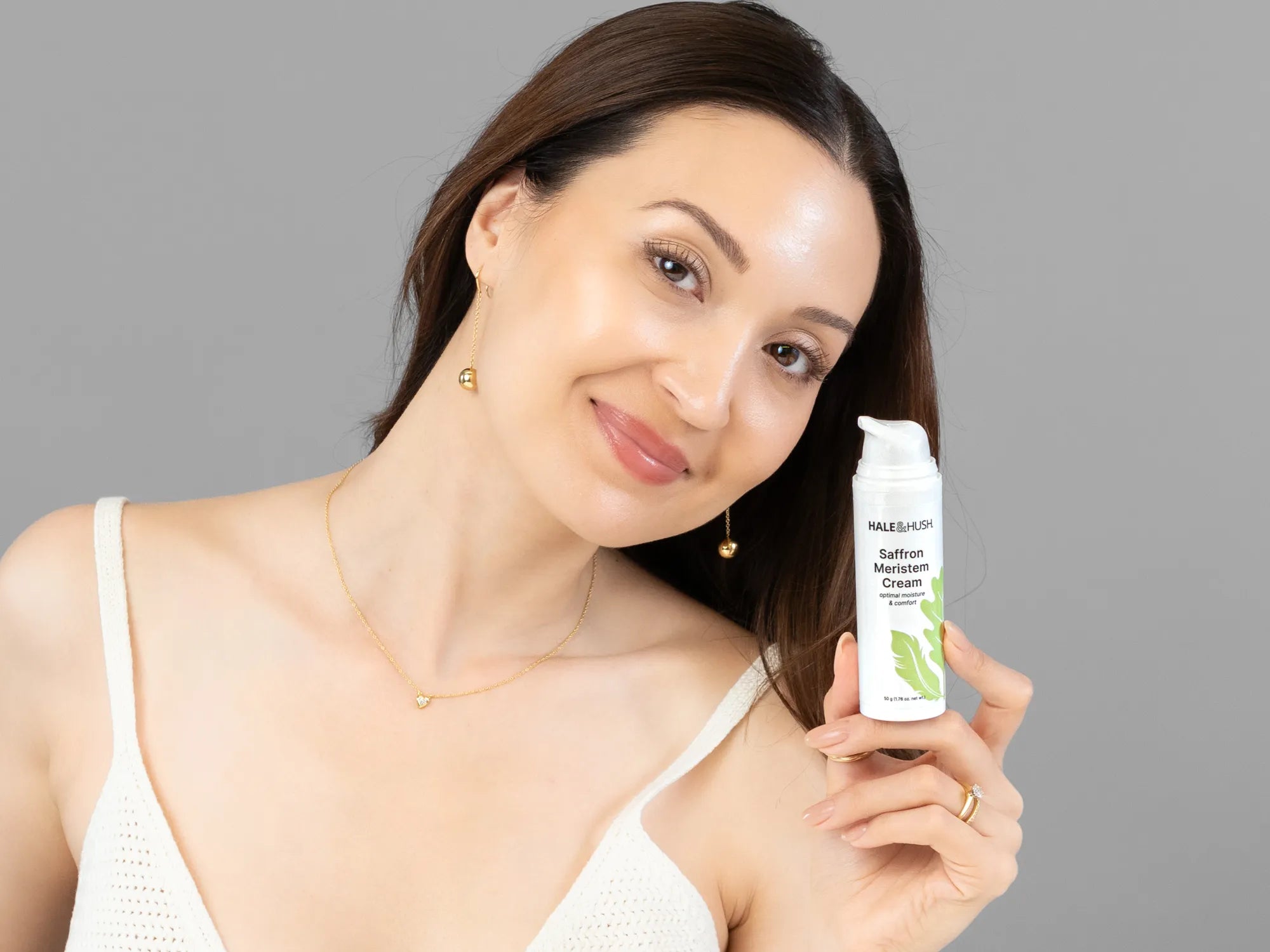 Laziza from LAZ Skincare holding a bottle of Hale & Hush Saffron Meristem Cream up to her face