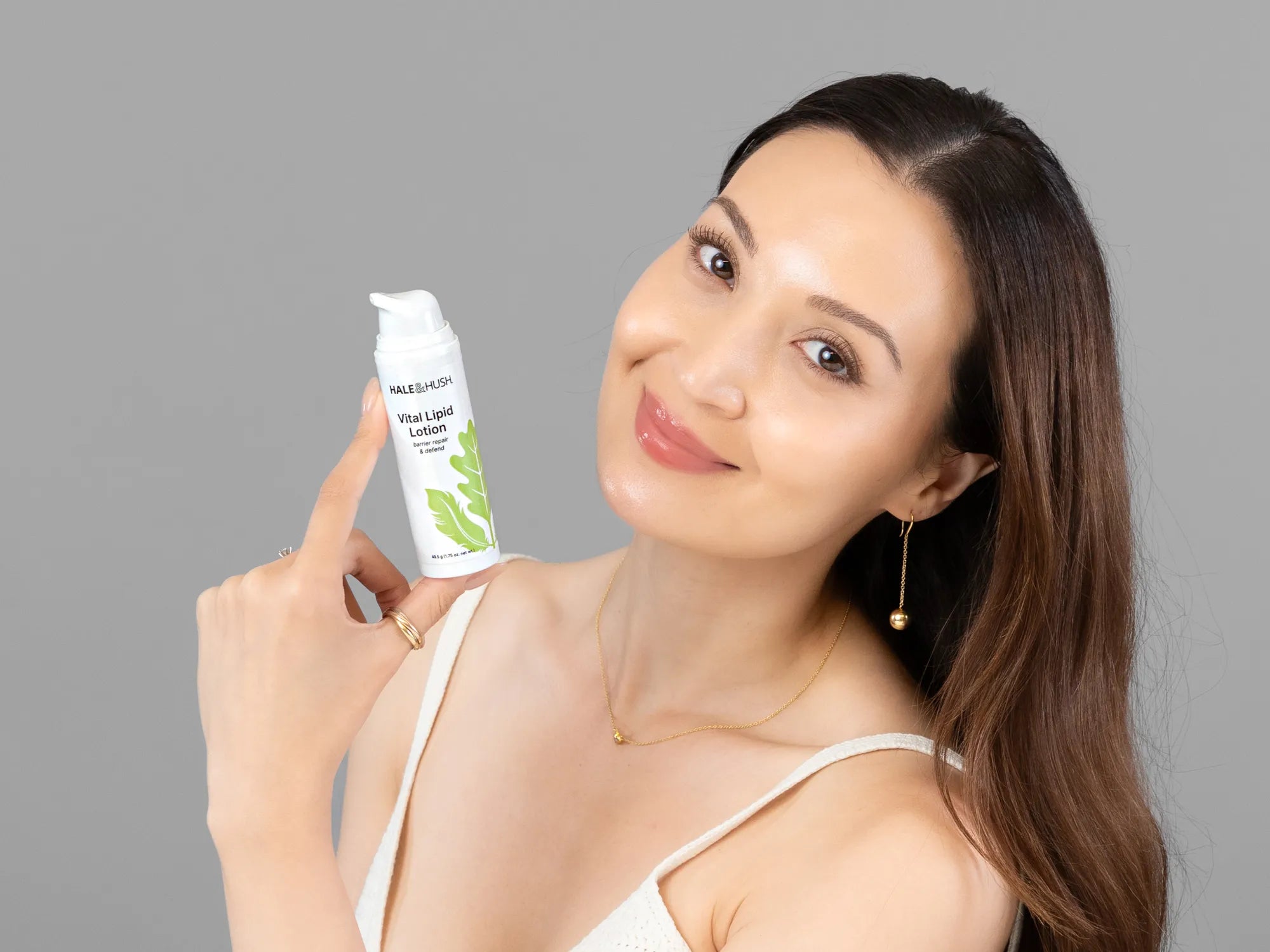 Laziza from LAZ Skincare holding a bottle of Hale & Hush Vital Lipid Lotion up to her face
