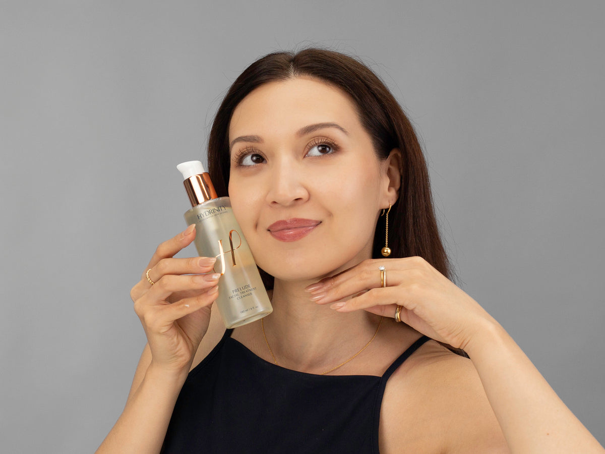 Laziza from LAZ Skincare holding a bottle of Hydrinity Prelude Facial Treatment Cleanser up to her face