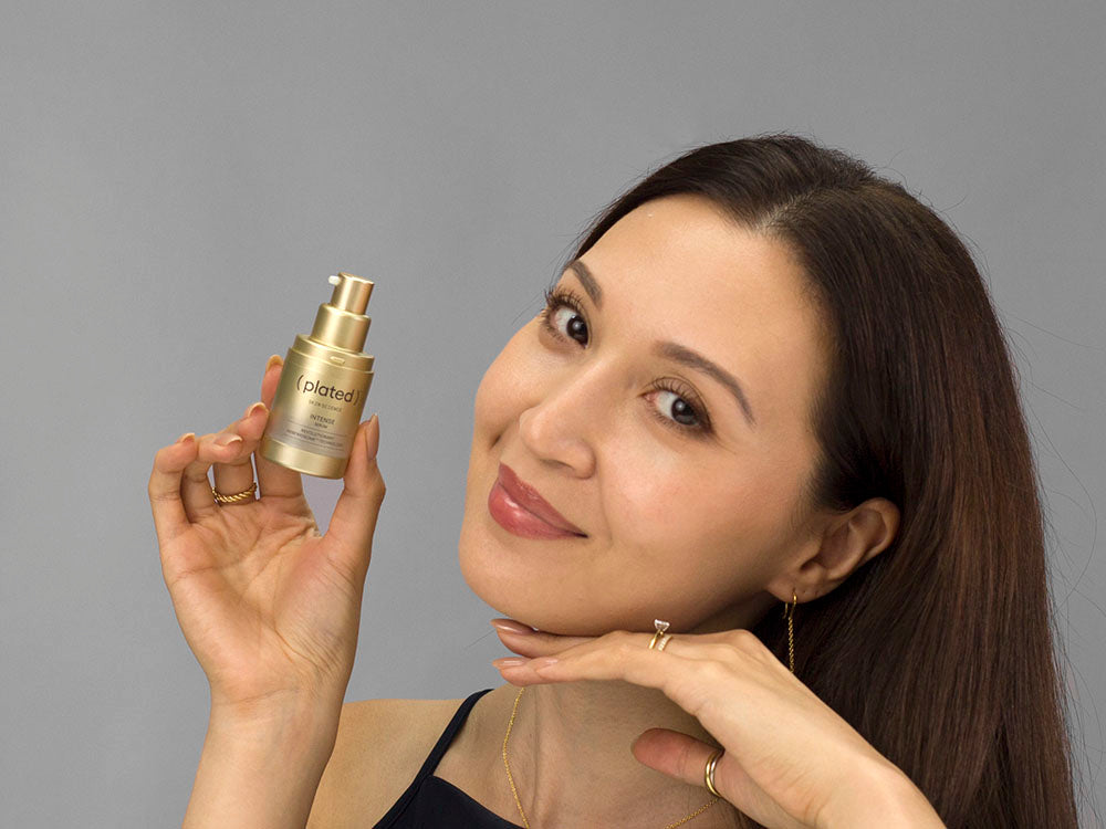 Laziza from LAZ Skincare holding a bottle of Plated Intense Serum up to her face