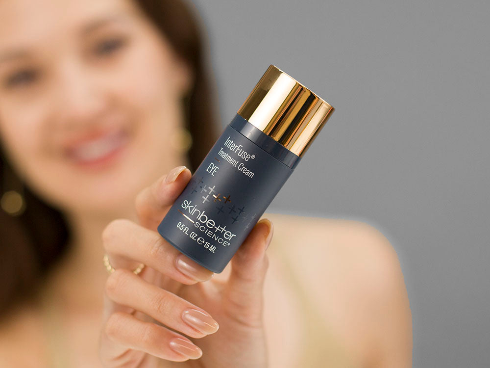 Laziza from LAZ Skincare holding a bottle of SkinBetter Science InterFuse Treatment Cream EYE up to her face
