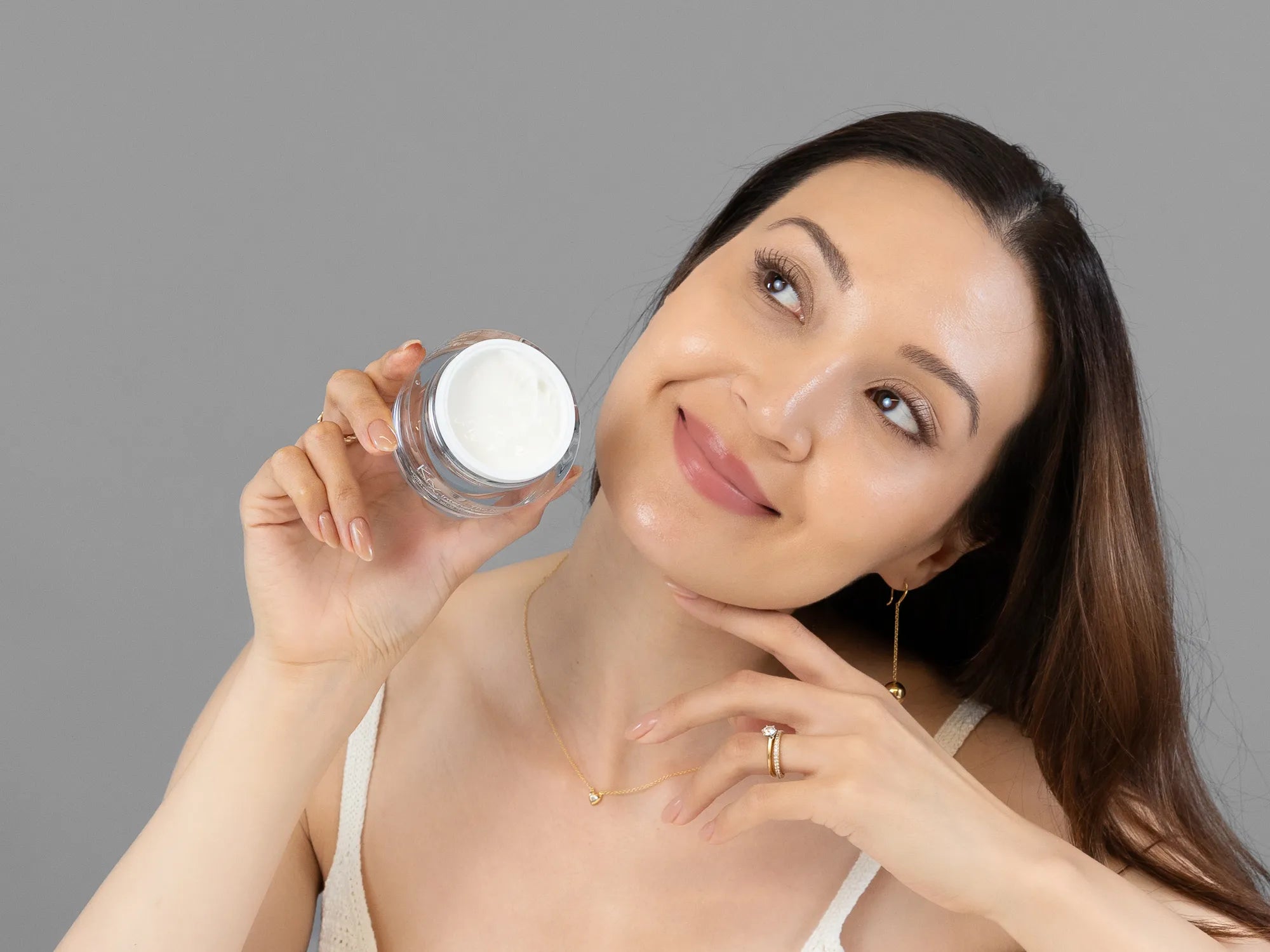 Laziza from LAZ Skincare holding a bottle of KrX Aesthetics Neck Lift Intensive Firming Cream up to her face