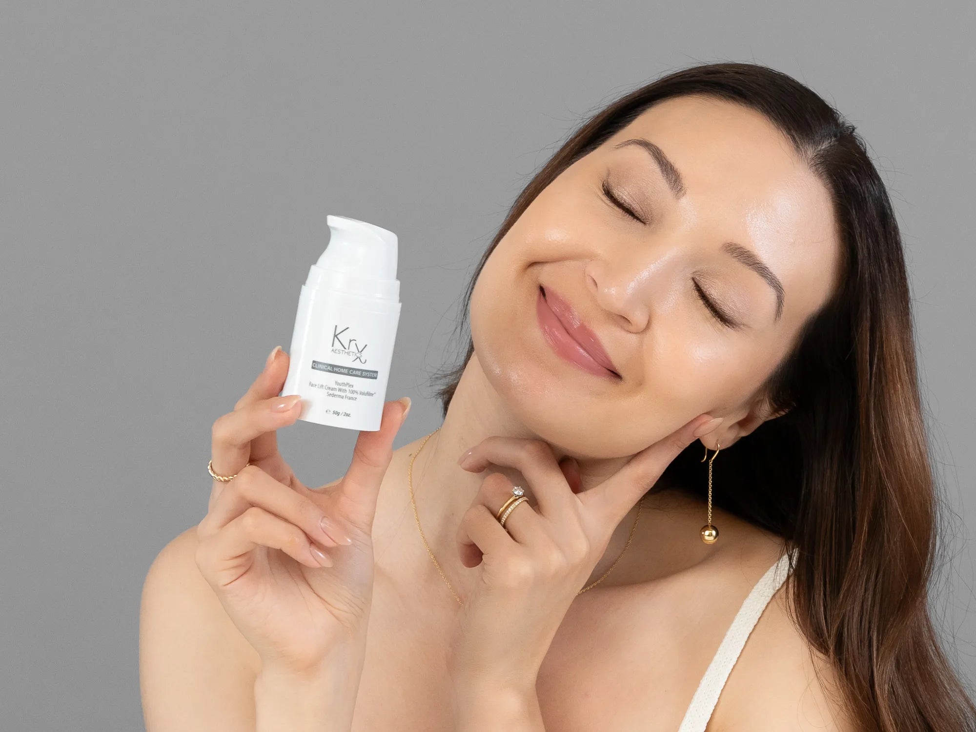 Laziza from LAZ Skincare holding a bottle of KrX Aesthetics Youthplex Face Lift Cream up to her face