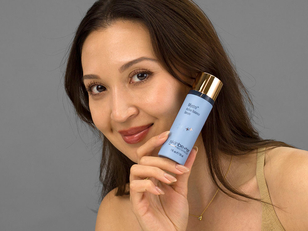 Laziza from LAZ Skincare holding a bottle of SkinBetter Science Mystro Active Balance Serum up to her face