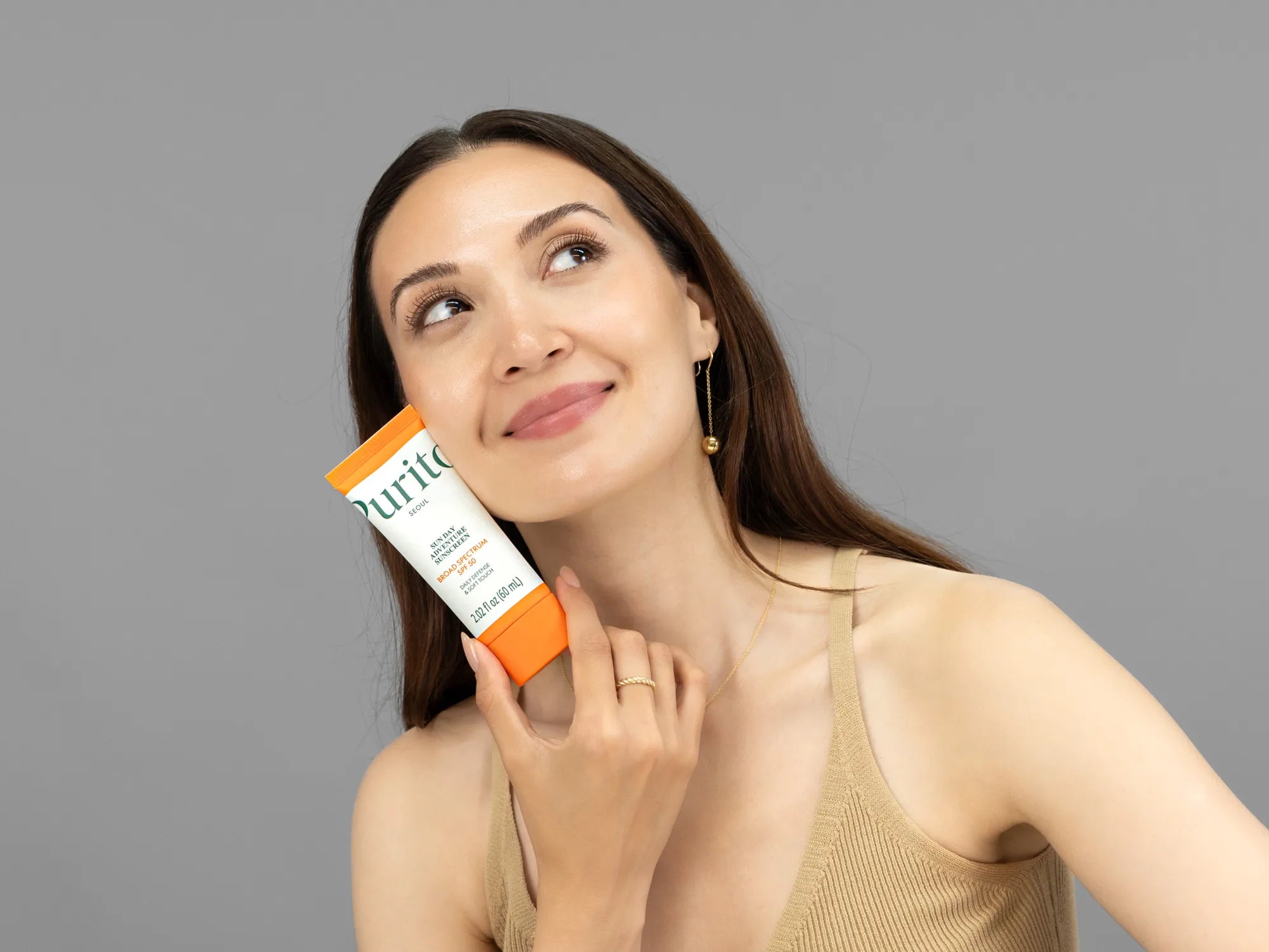 Laziza from LAZ Skincare holding a bottle of Purito Seoul Sun Day Adventure Sunscreen up to her face