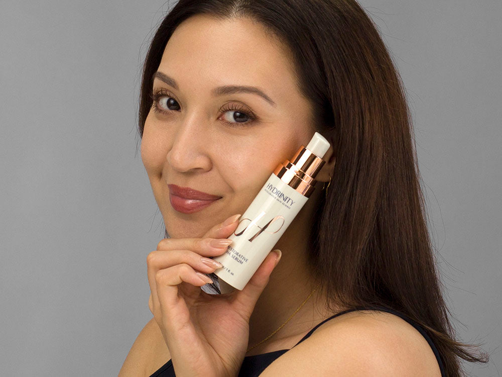 Laziza from LAZ Skincare holding a bottle of Hydrinity Renewing HA Serum up to her face