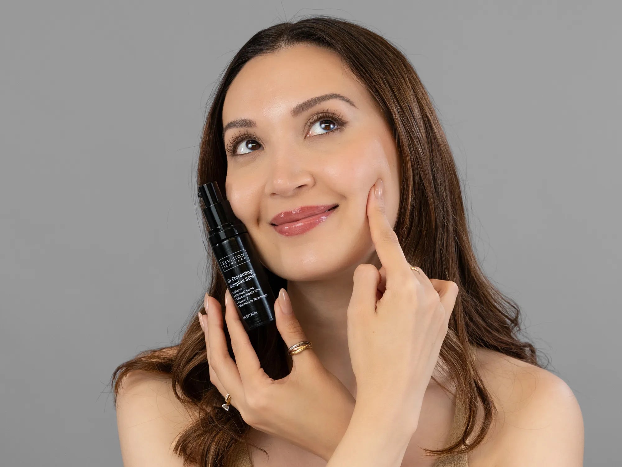 Laziza from LAZ Skincare holding a bottle of Revision C+ Correcting Complex 30% up to her face