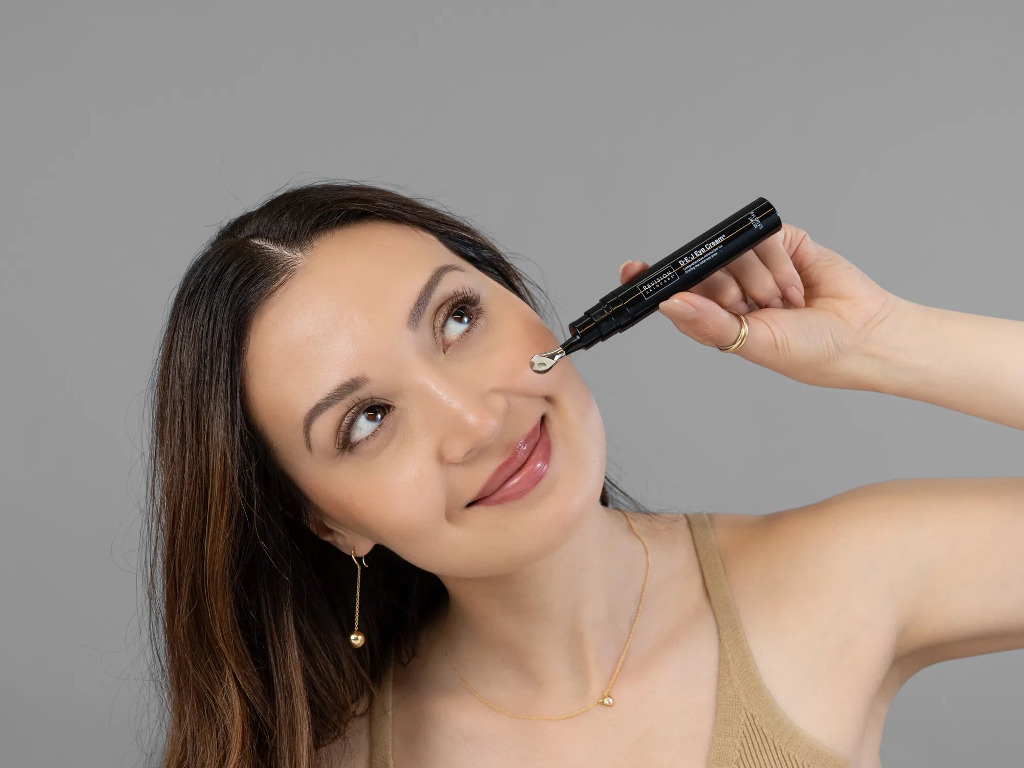 Laziza from LAZ Skincare holding a bottle of Revision D·E·J Eye Cream up to her face