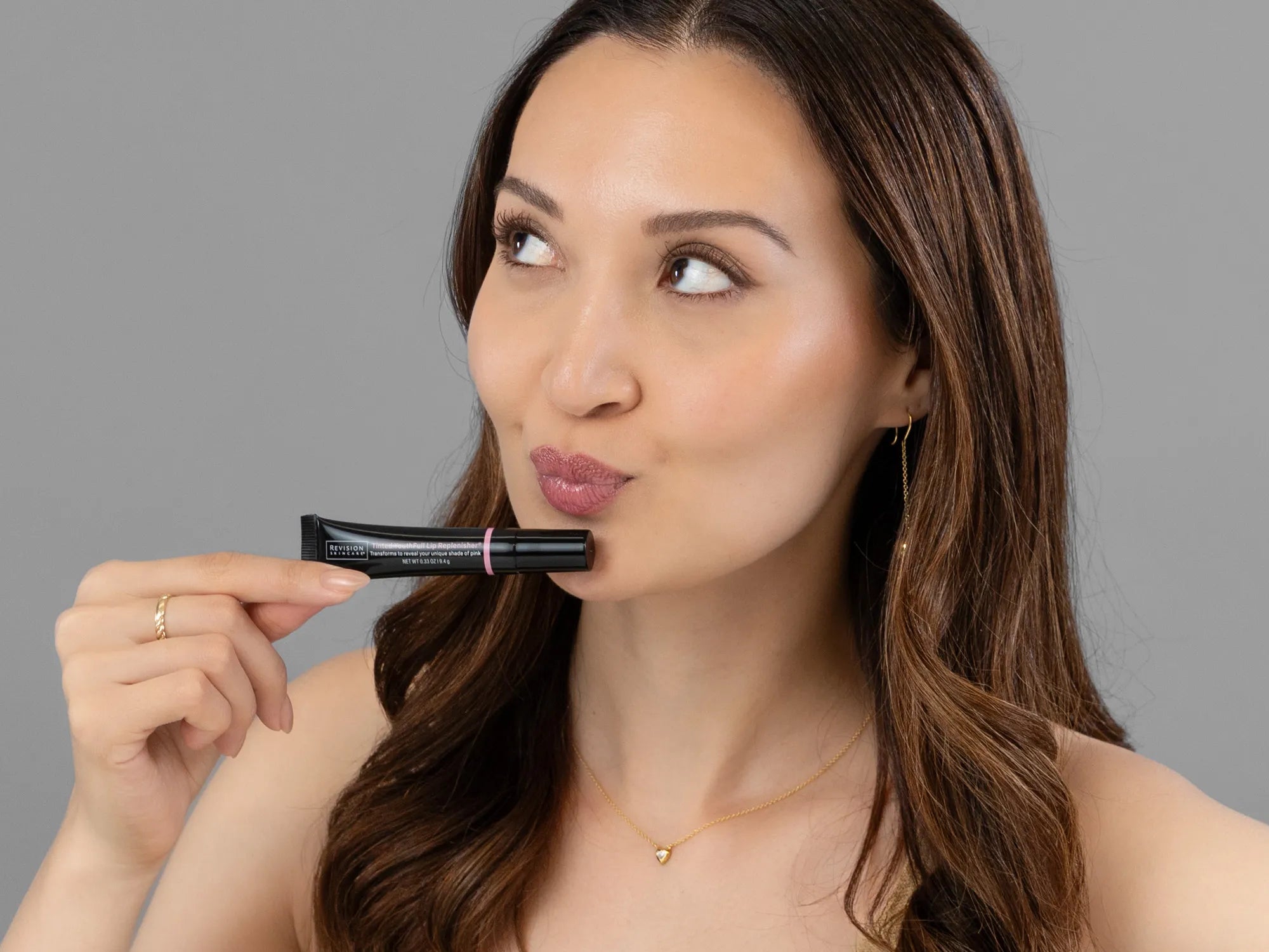 Laziza from LAZ Skincare holding a bottle of Revision Youthfull Lip Replenisher up to her face