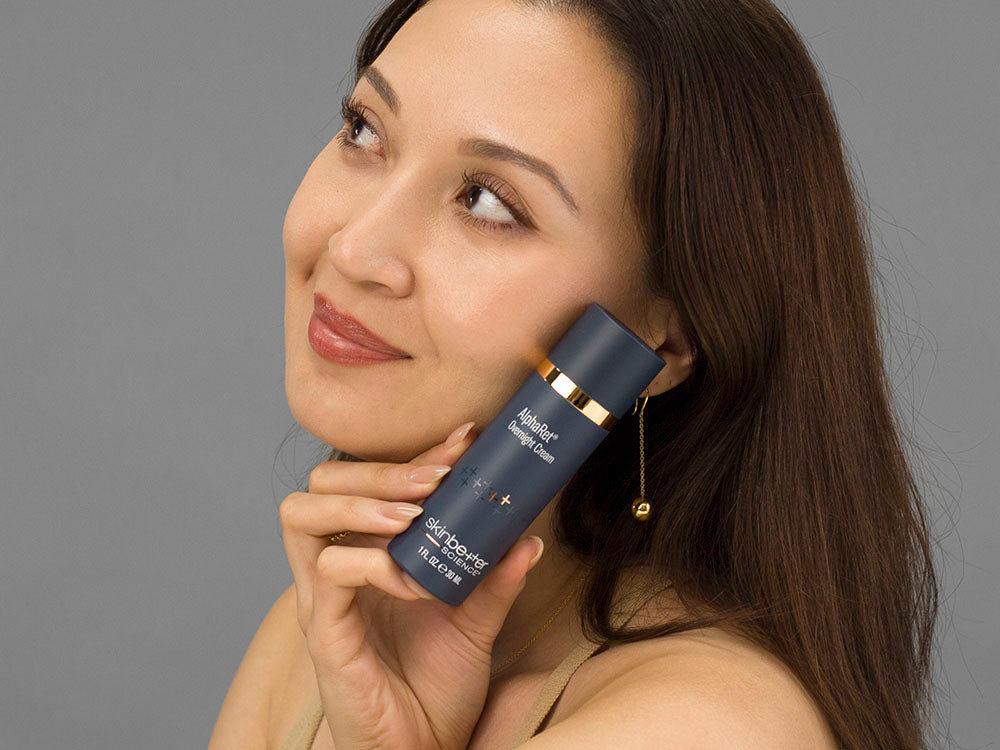 Laziza from LAZ Skincare holding a bottle of SkinBetter Science AlphaRet Overnight Cream up to her face