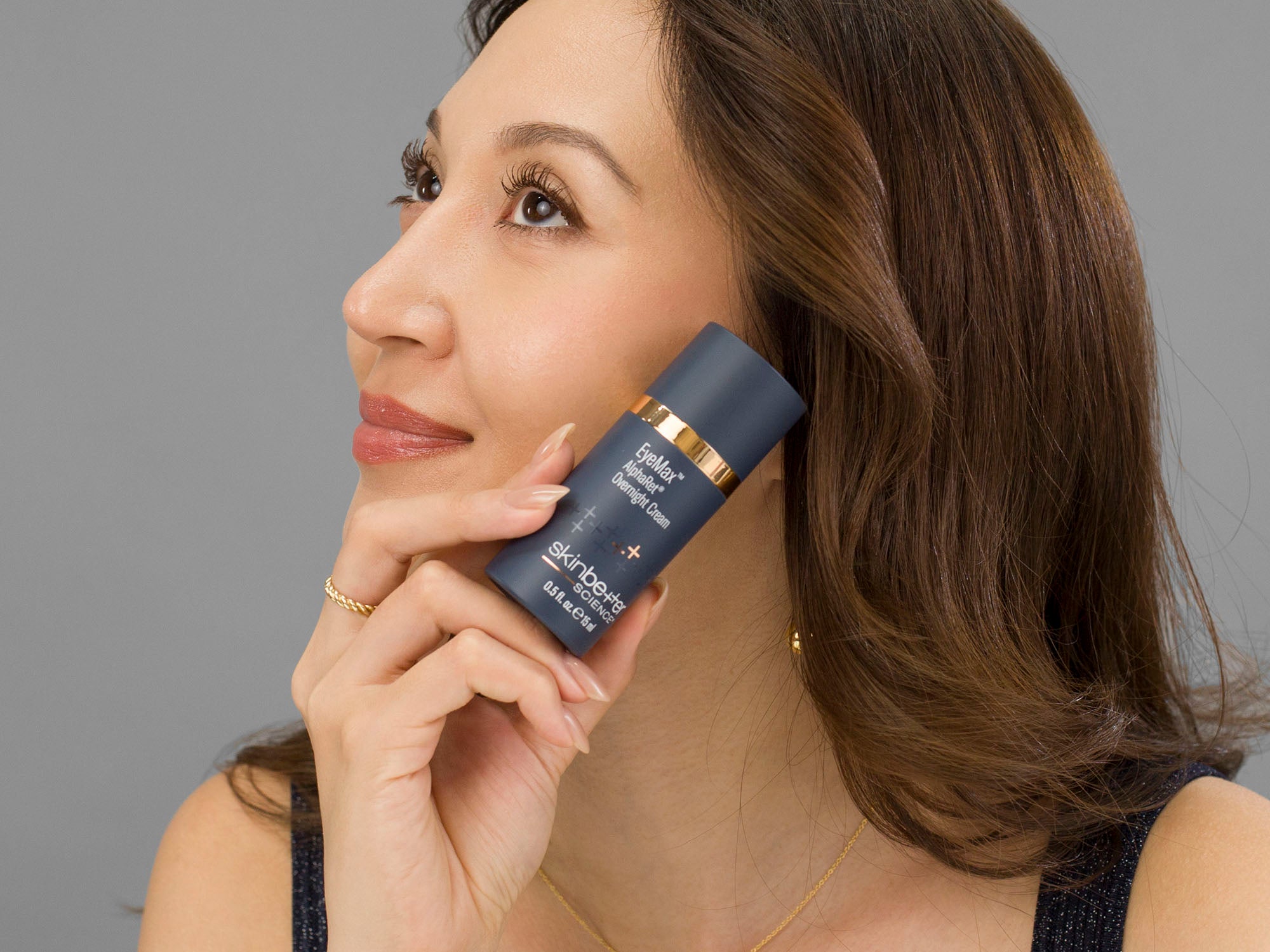 Laziza from LAZ Skincare holding a bottle of Skinbetter Science EyeMax AlphaRet Overnight Cream up to her face