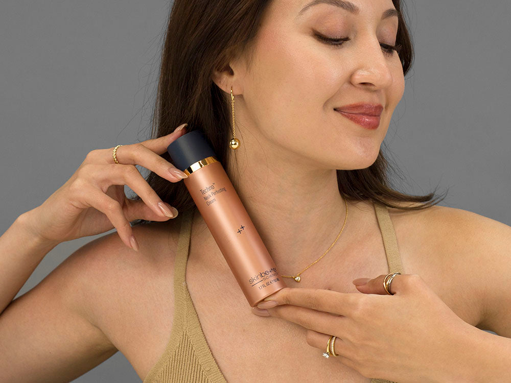 Laziza from LAZ Skincare holding a bottle of Skinbetter Science Techno Neck Perfecting Cream up to her neck