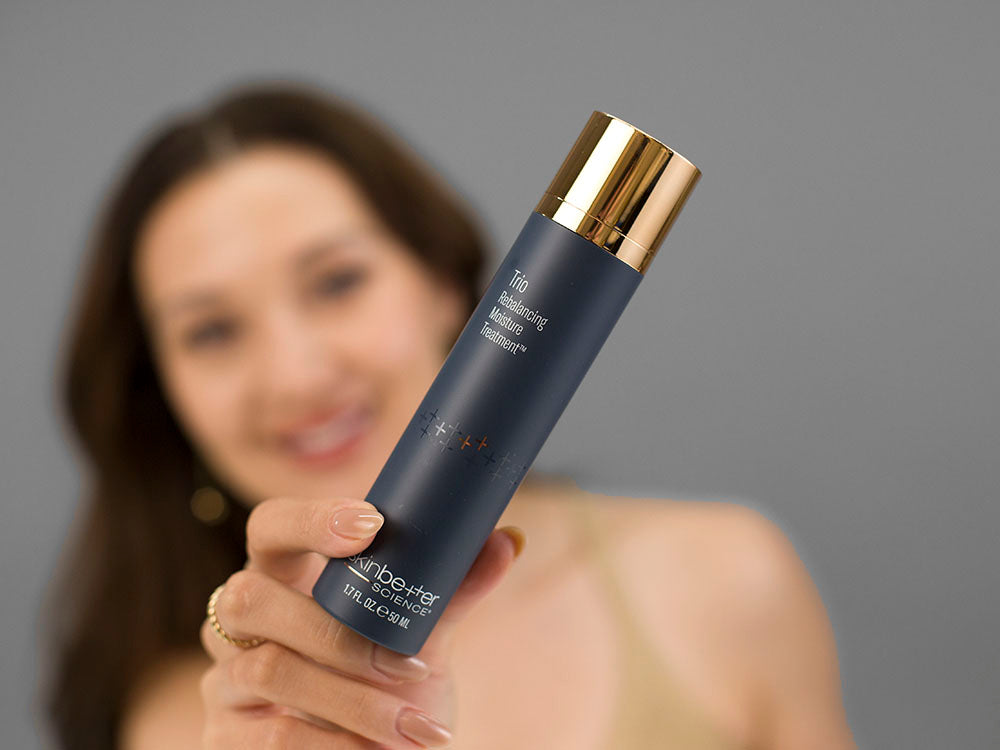 Laziza from LAZ Skincare holding a bottle of SkinBetter Science Trio Rebalancing Moisture Treatment up to her face