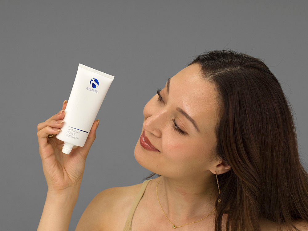 Laziza from LAZ Skincare holding a bottle of iS Clinical Warming Honey Cleanser up to her face