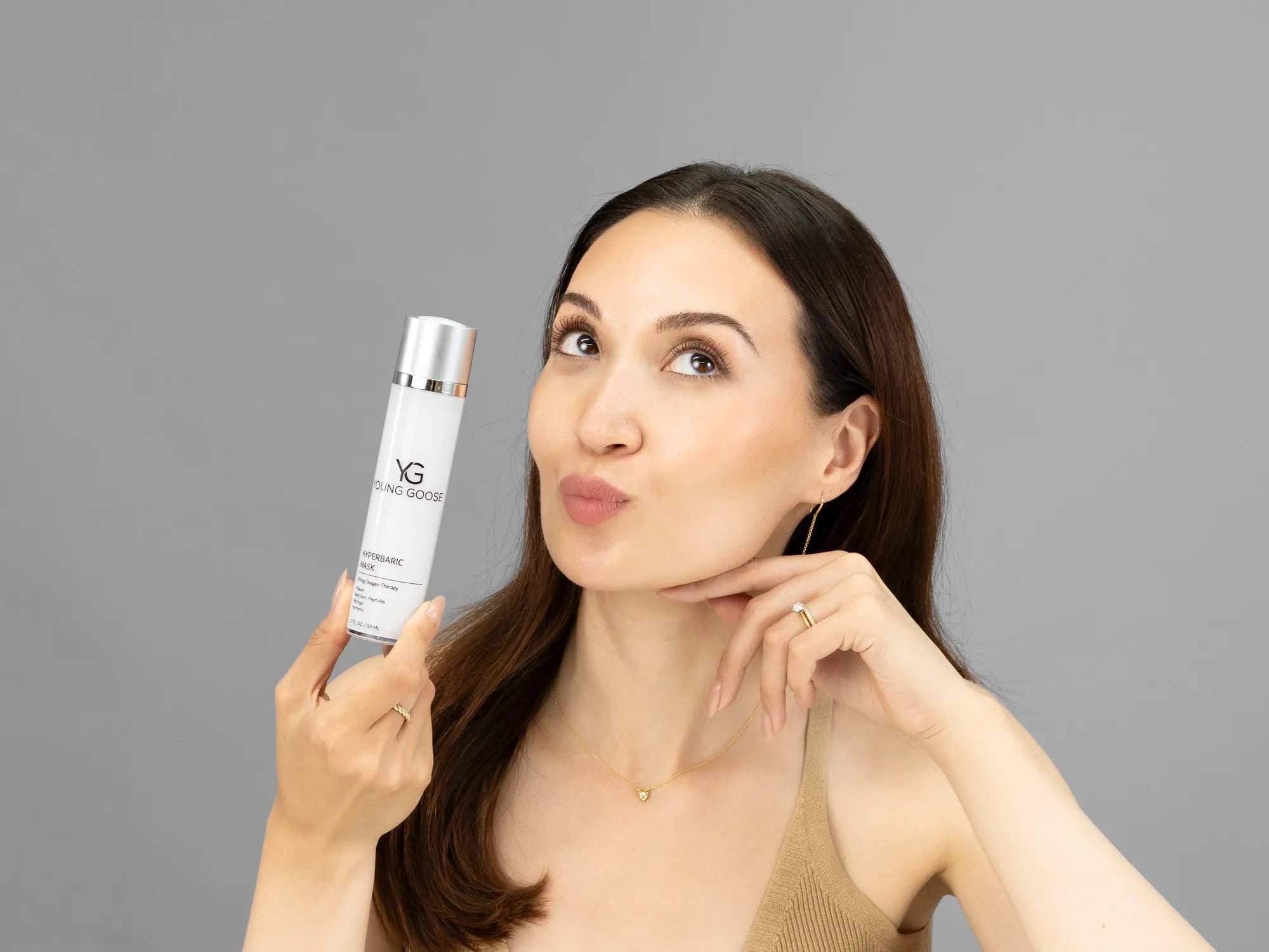 Laziza from LAZ Skincare holding a bottle of Young Goose Hyperbaric Mask up to her face
