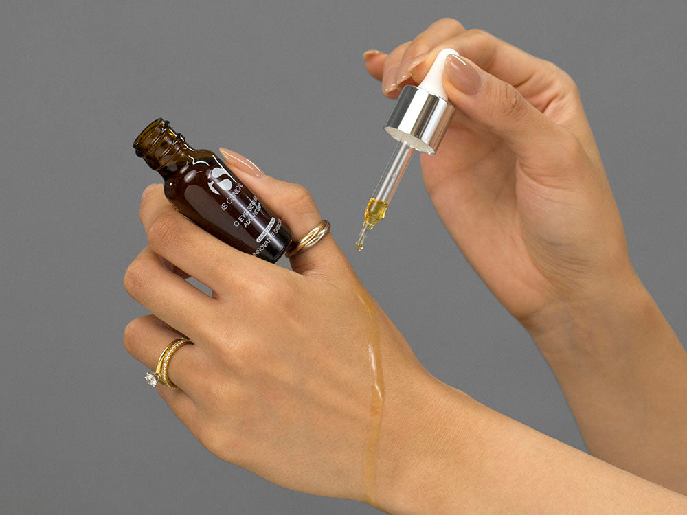 Closeup of Laziza from LAZ Skincare applying the spray from a bottle of iS Clinical C Eye Serum Advance to her hand with a dropper