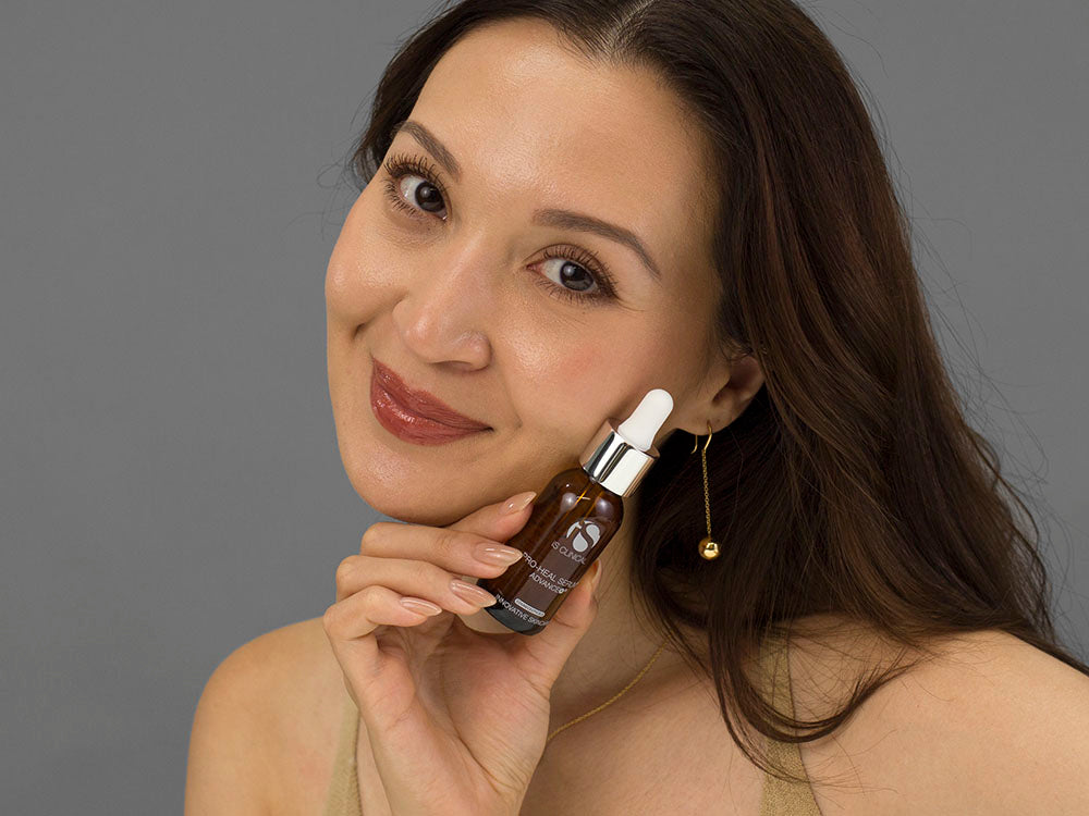 Laziza from LAZ Skincare holding a bottle of iS Clinical Pro-Heal Serum Advance up to her face